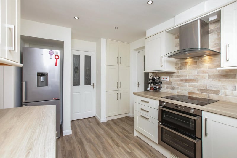 Integrated appliances include a dishwasher, an electric oven with induction hob and a stainless steel chimney-style extractor fan above, while there is space for a fridge/freezer.