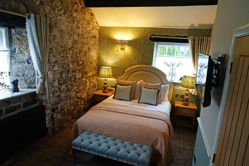Dusky pink soft furnishings add a feminine touch in The Dale End bedroom which has an exposed stone wall.