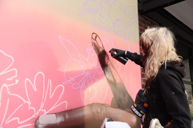 Peachzz creating her mural of the hands of the community holding up local flowers.