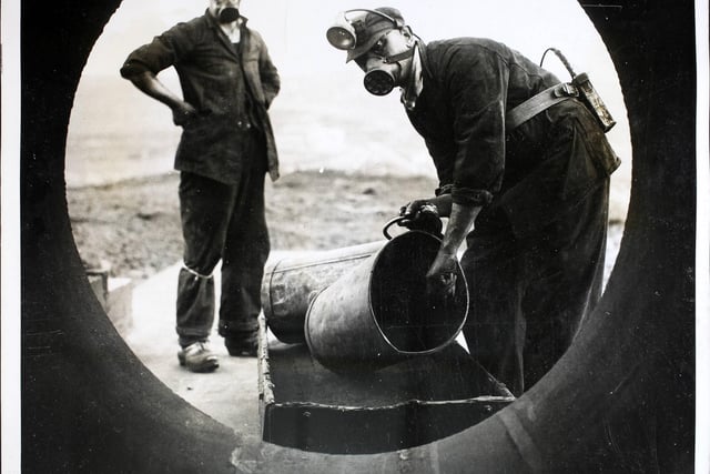 Men wearing respirators loading a four-foot wide tube with coal dust on a hilltop at Harpur Hill, Derbyshire, before detonating it in a controlled explosion for an experiment. (Photo by Fox Photos/Hulton Archive/Getty Images)
