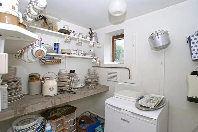 The pantry, which contains shelving and a stone slab and has space for a fridge, is located off the kitchen.