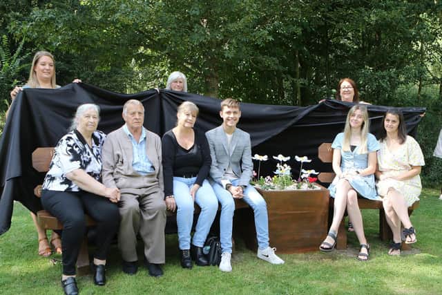 Nicola and family of her late husband Ian on the new seat. Community Unity Project's Zara Skidmore, April Johnson and Elaine Streets are holding the sheet at the back.