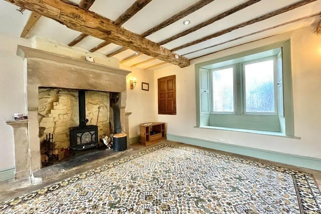 A stone fireplace housing a wood burning stove, flagstone flooring, original wall cupboard, wooden window shutters incoporating a window seat and ceiling beams give olde-worlde character to this charming room.