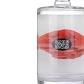 The back of the bottle displays a poppy containing a QR code to hear the song