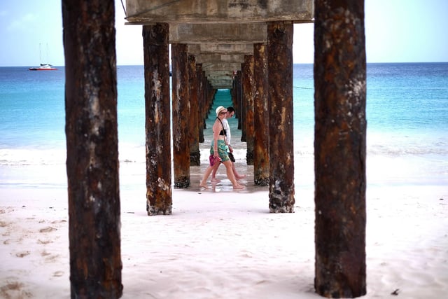 Two tourists walk under a jetty as they stroll along a beach in Bridgetown, Barbados - flights bound for Bridgetown take off from Doncaster Sheffield Airport.