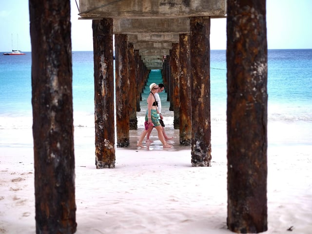 Two tourists walk under a jetty as they stroll along a beach in Bridgetown, Barbados - flights bound for Bridgetown take off from Doncaster Sheffield Airport.