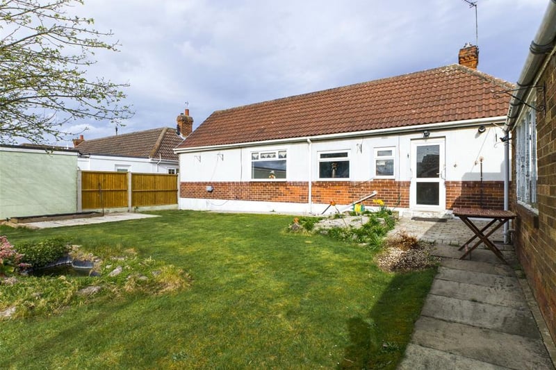 Enclosed rear garden laid to lawn with paved path, boundary hedge, garden pond, tool shed and plants and shrubs.