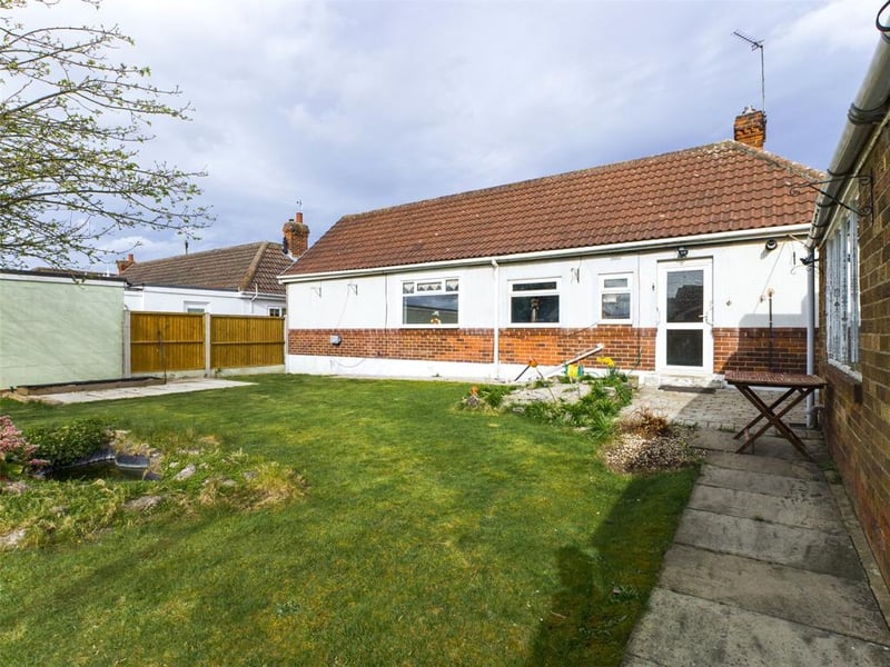 Enclosed rear garden laid to lawn with paved path, boundary hedge, garden pond, tool shed and plants and shrubs.