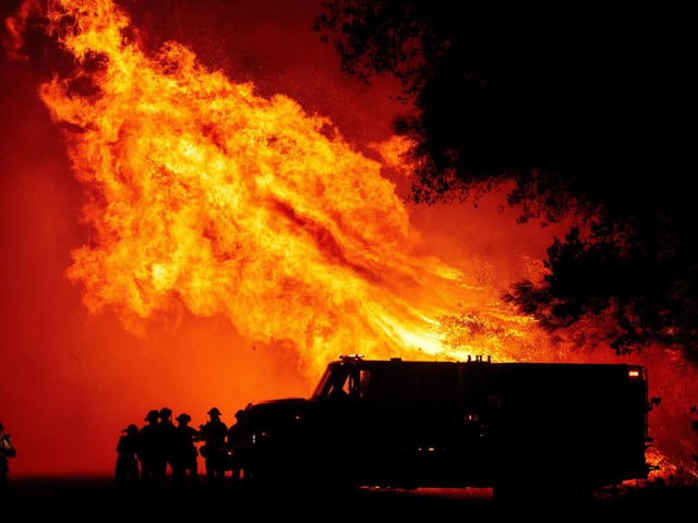 Butte county firefighters watch as flames tower over their truck during the Bear fire in Oroville.