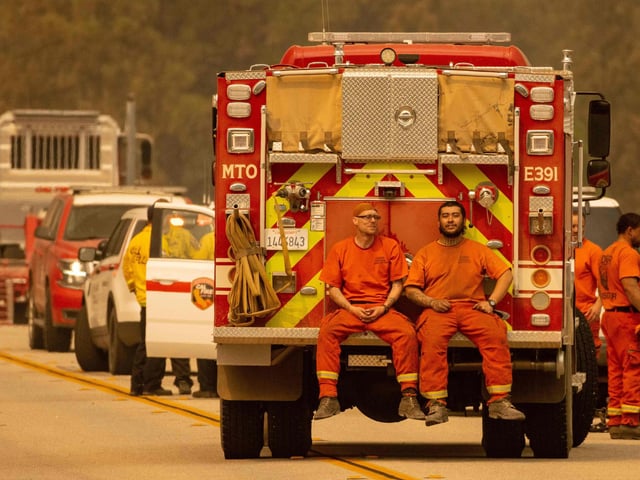 Firefighters sit on the back of a fire truck on the Enterprise Bridge