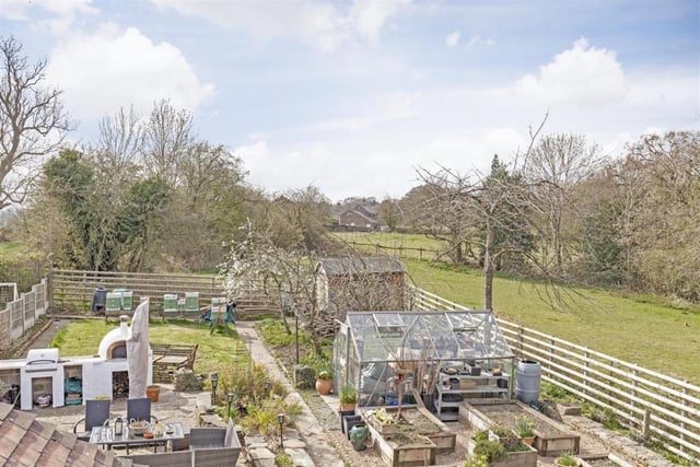 The rear garden has raised vegetable beds, a lawned area, is fenced and is bordered by open fields.