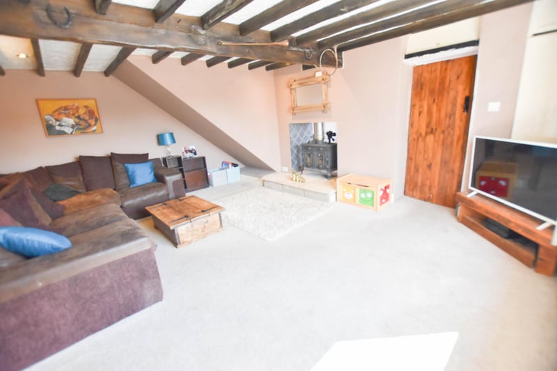 A spacious lounge with carpet flooring and decorated in earth tones. Feature log burner shared with kitchen/diner and window. Door to storage cupboard.