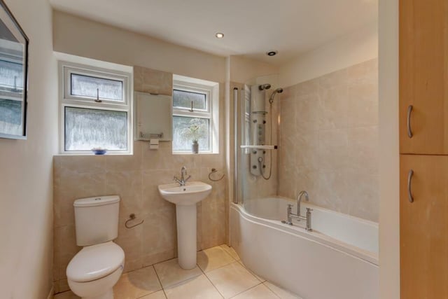 The bath has a fitted shower panel incorporating a shower, an additional hand shower facility and body jets. There is a storage cupboard with shelving in one corner of the room.