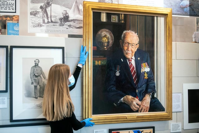 A staff member adjusts a portrait of Captain Sir Tom Moore by artist Alex Chamberlin, as it is unveiled at the National Army Museum in Chelsea, London to mark the 75th anniversary of VJ day.