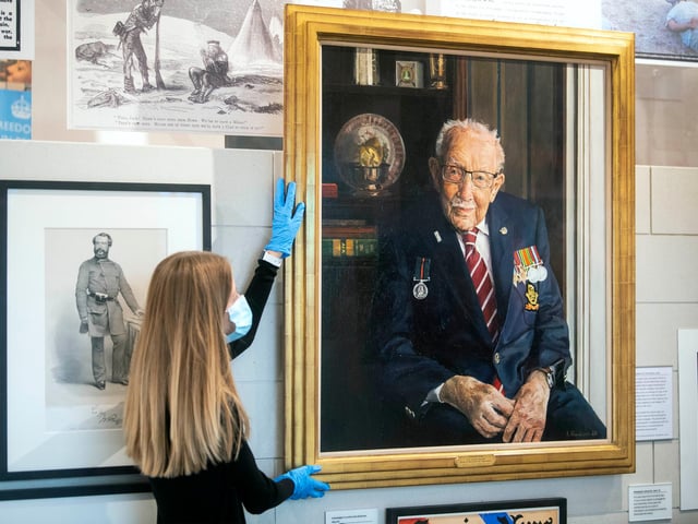 A staff member adjusts a portrait of Captain Sir Tom Moore by artist Alex Chamberlin, as it is unveiled at the National Army Museum in Chelsea, London to mark the 75th anniversary of VJ day.