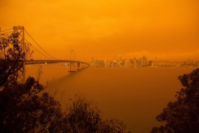 The San Francisco Bay Bridge and city skyline are obscured in orange smoke.