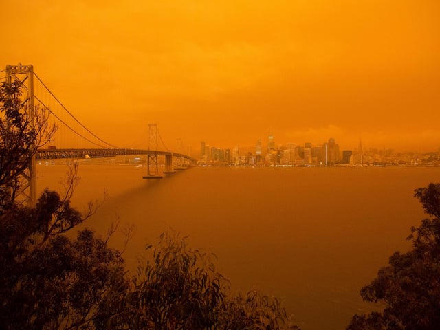 The San Francisco Bay Bridge and city skyline are obscured in orange smoke.