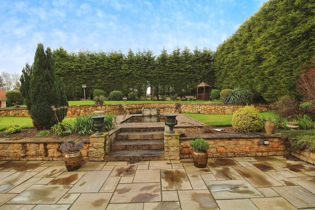 The £900,000 property is surrounded by extensive, landscaped gardens. This is the rear, where there is a large patio, a fish pond, flowerbeds and conifers.